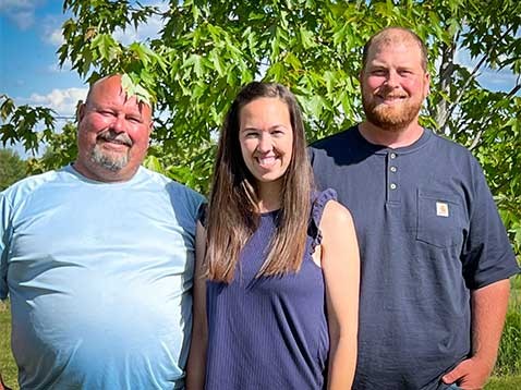 Two men and a woman standing by a tree smiling